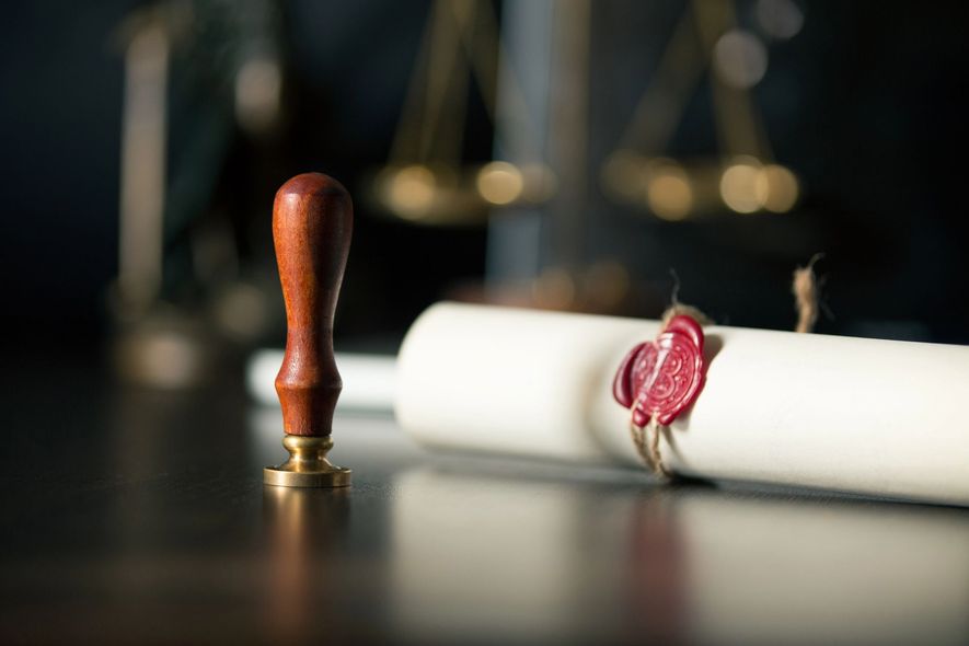 Una pergamena sigillata con ceralacca accanto a un timbro di legno su un tavolo scuro.