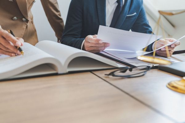 Persone che esaminano documenti attorno a un tavolo da conferenza con un libro aperto e un computer portatile.