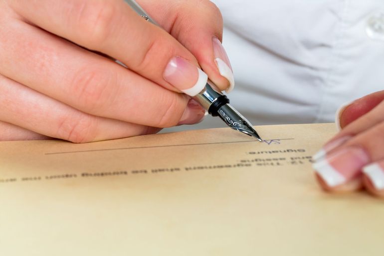 Firmare a mano un documento con una penna su un modulo beige