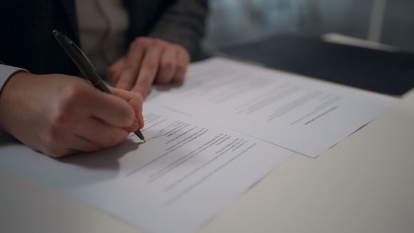 Mano che firma un documento su una scrivania con una penna, vista ravvicinata