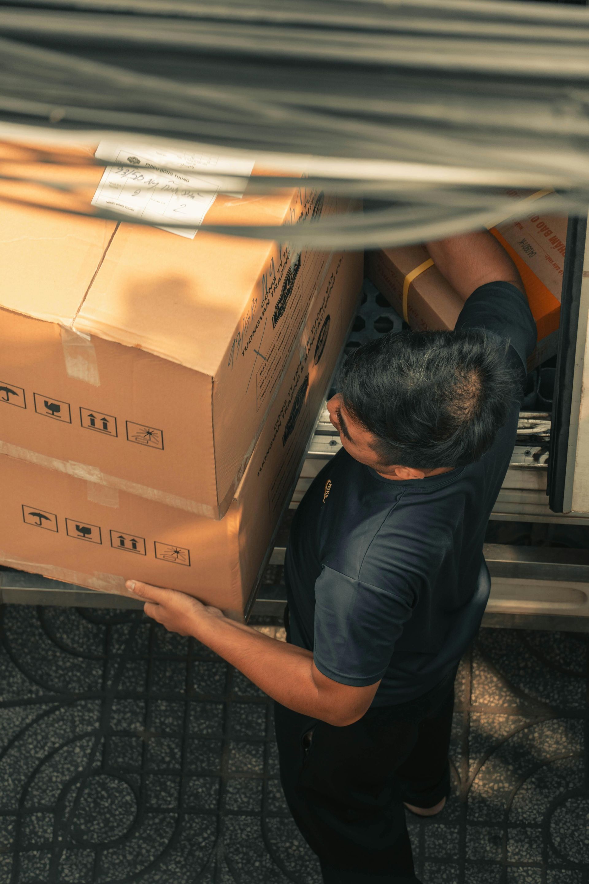 Person carrying stacked cardboard boxes beside a vehicle in an outdoor setting