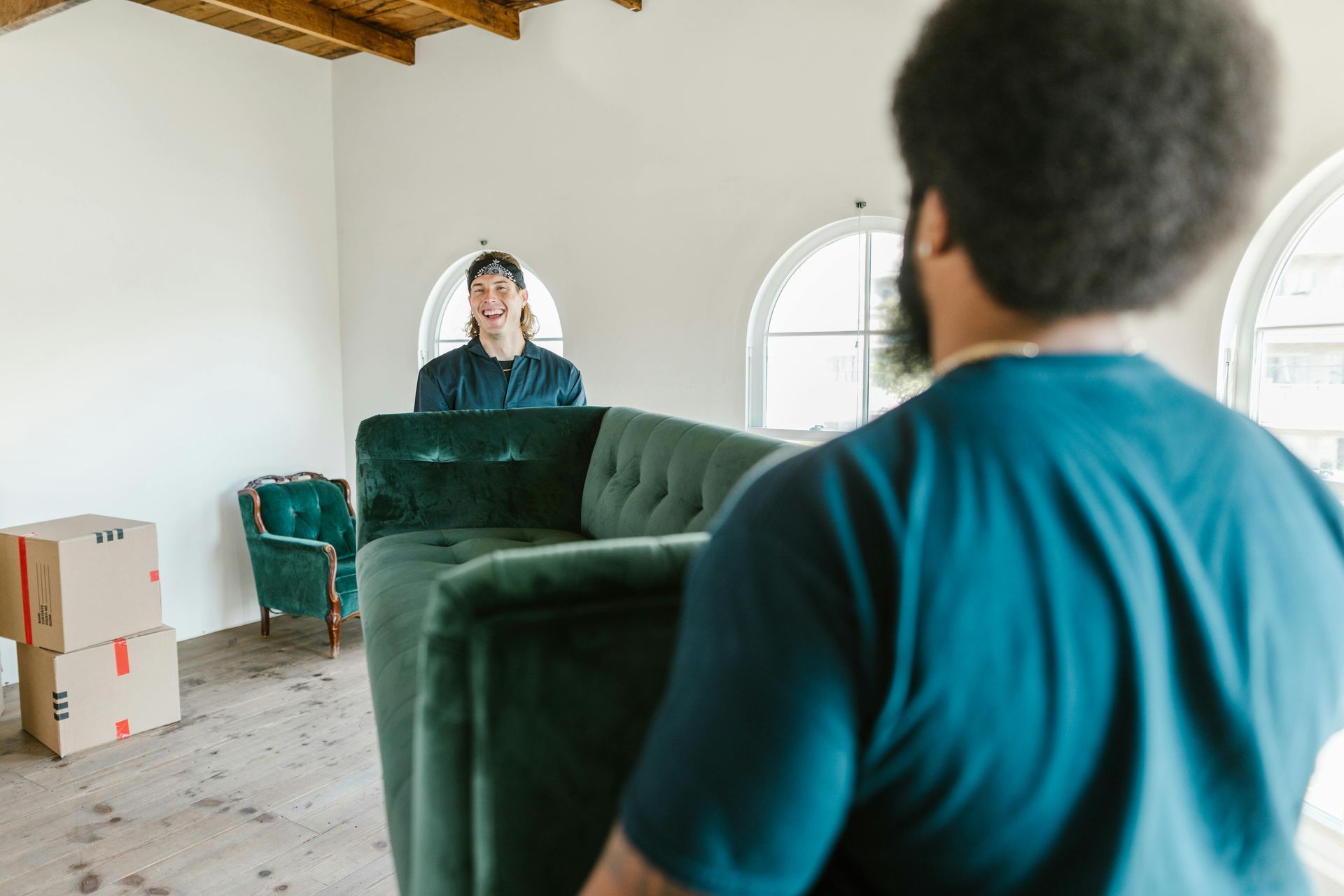 Person in teal shirt looks into a mirror in a sparsely furnished room with boxes and a green couch.