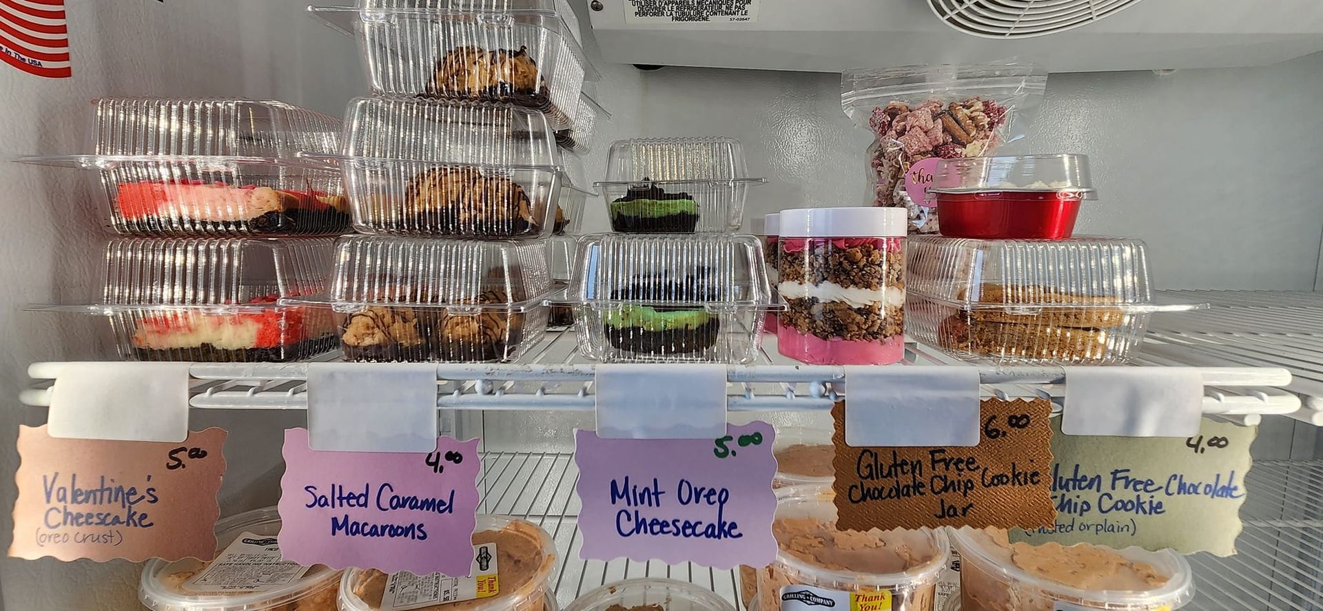 A variety of desserts are displayed in plastic containers on a shelf.
