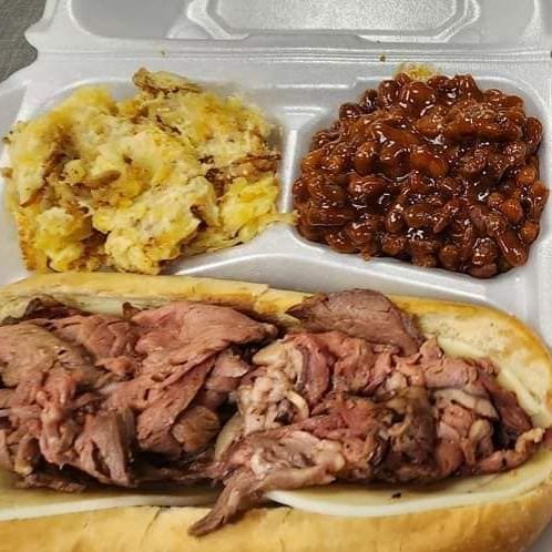 A styrofoam container filled with a sandwich , beans , and eggs.