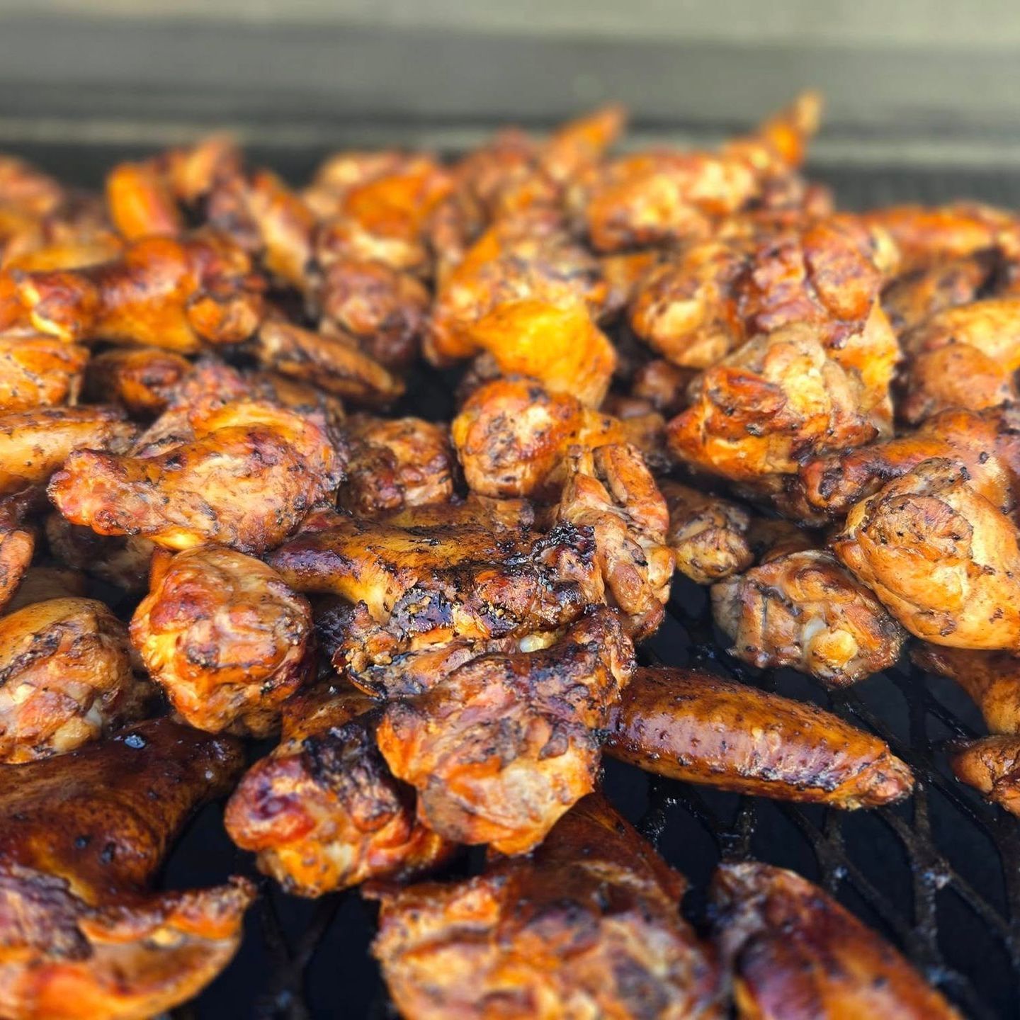 A bunch of chicken wings are cooking on a grill.