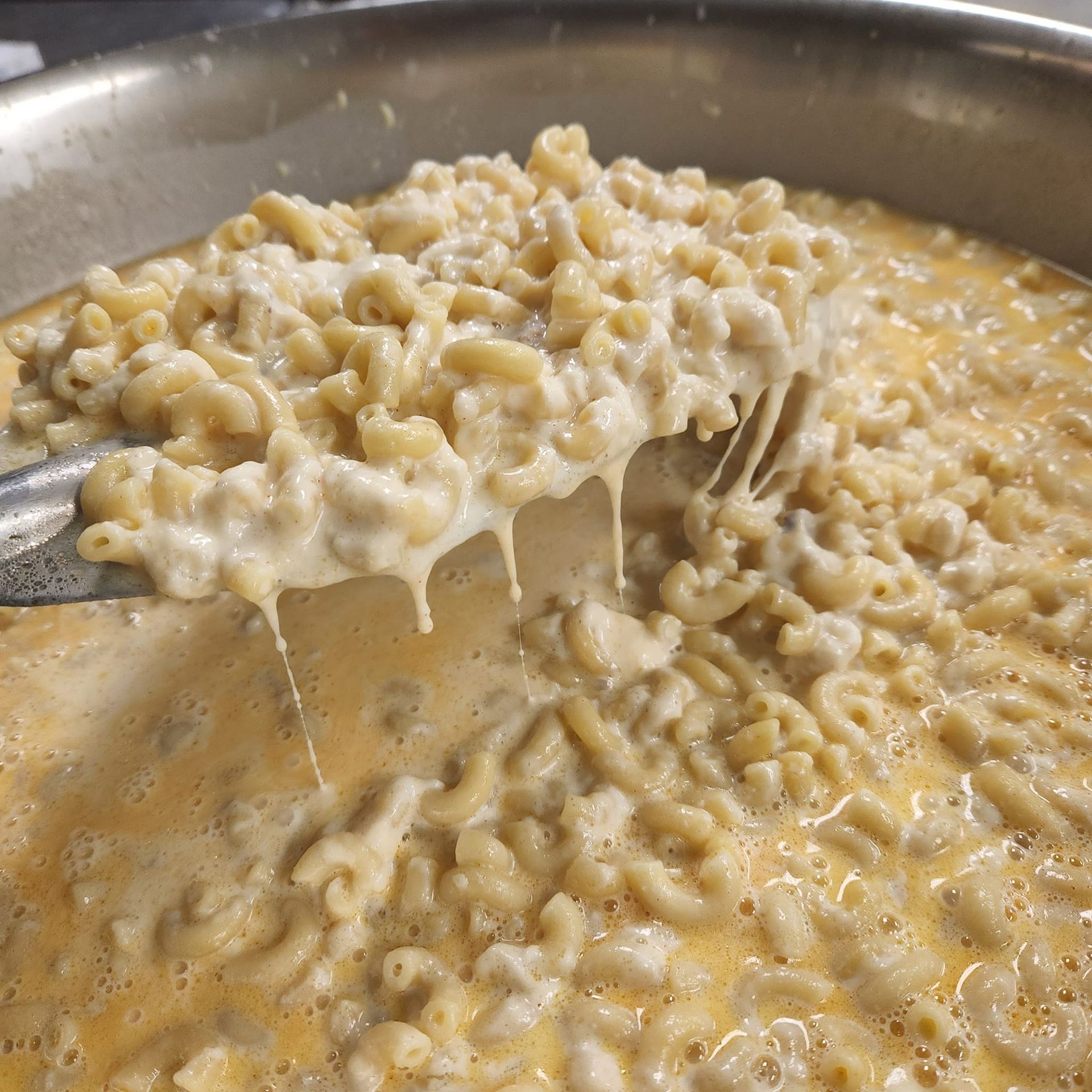 Macaroni and cheese is being scooped out of a pot with a fork.