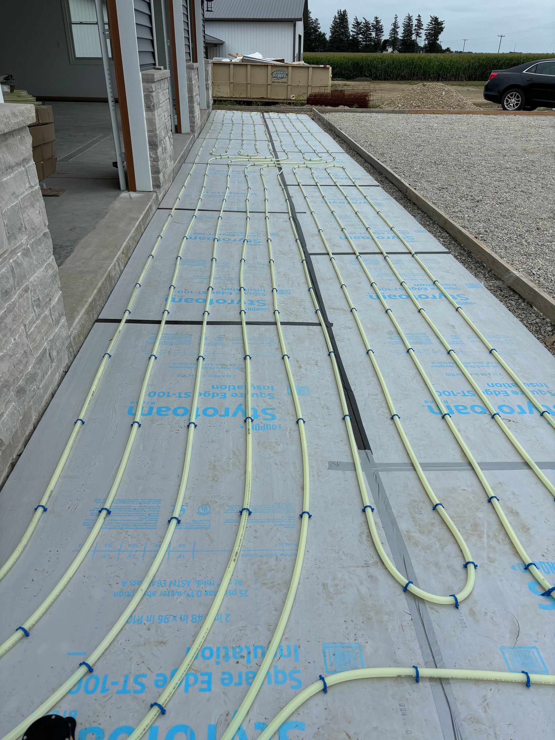 Yellow tubing laid on insulation, likely for radiant floor heating, outside a building.