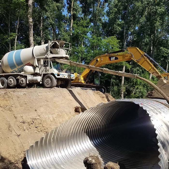 Construction site with cement truck, excavator, and large corrugated culvert pipe being installed