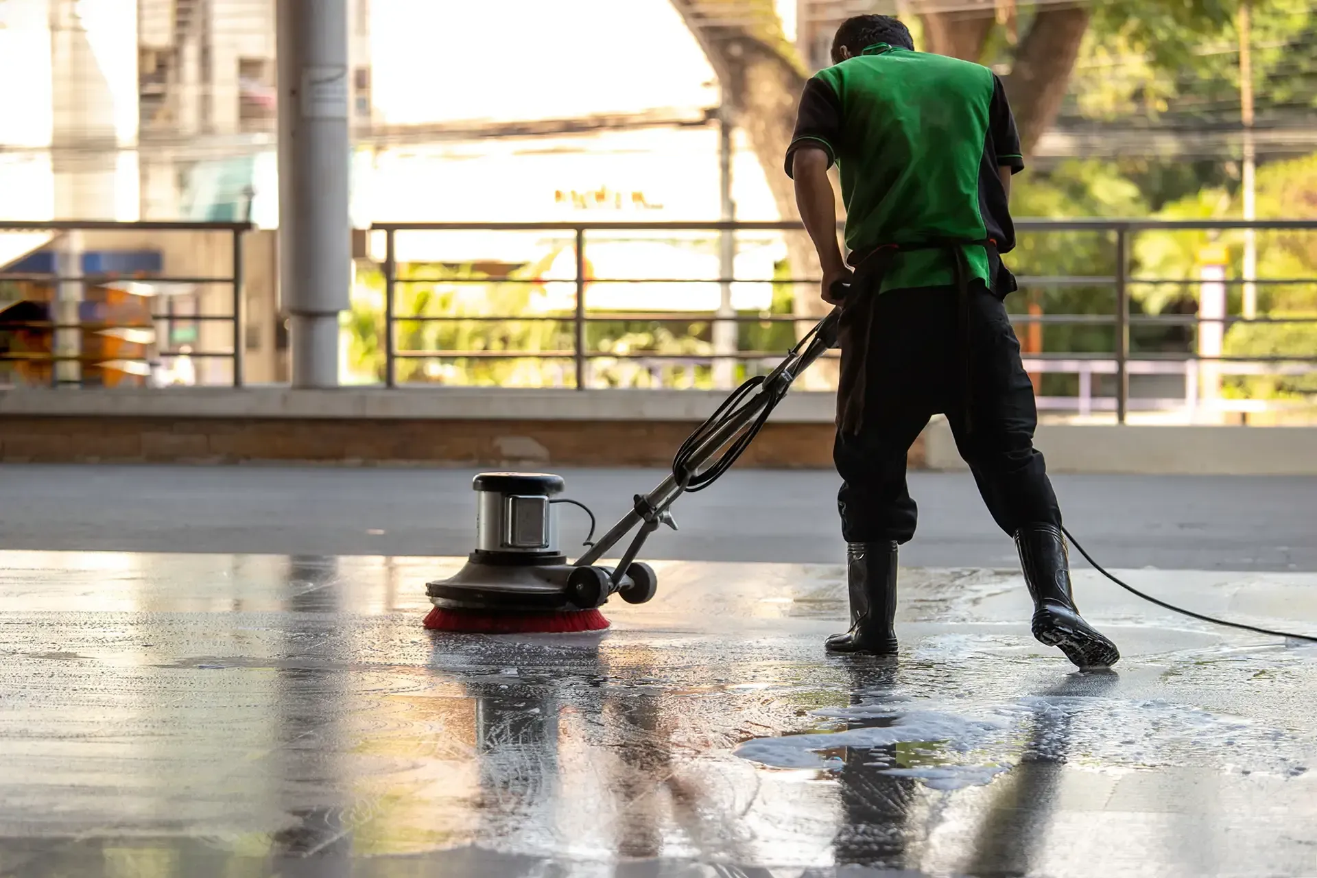 Person in green shirt cleans a wet, reflective floor with an industrial floor buffer.