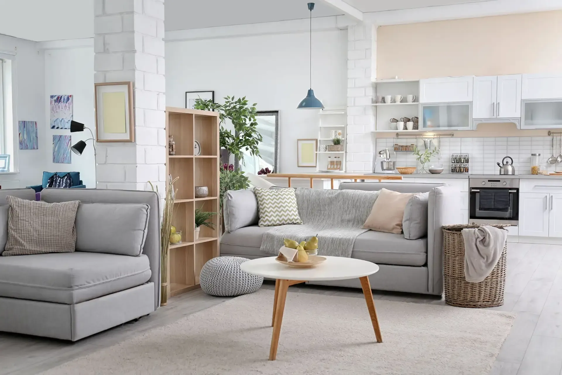 Spacious living area with gray sofas, wooden shelving, and open-plan kitchen with white cabinetry.