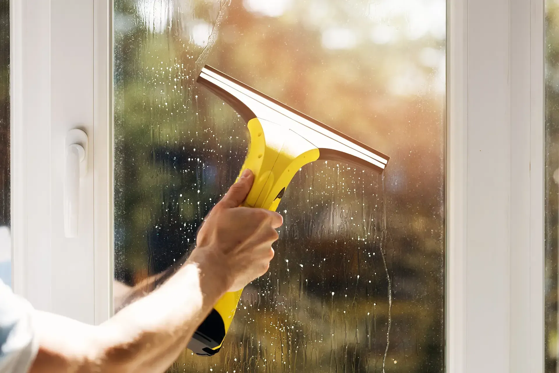 Person cleaning a window with a yellow squeegee.