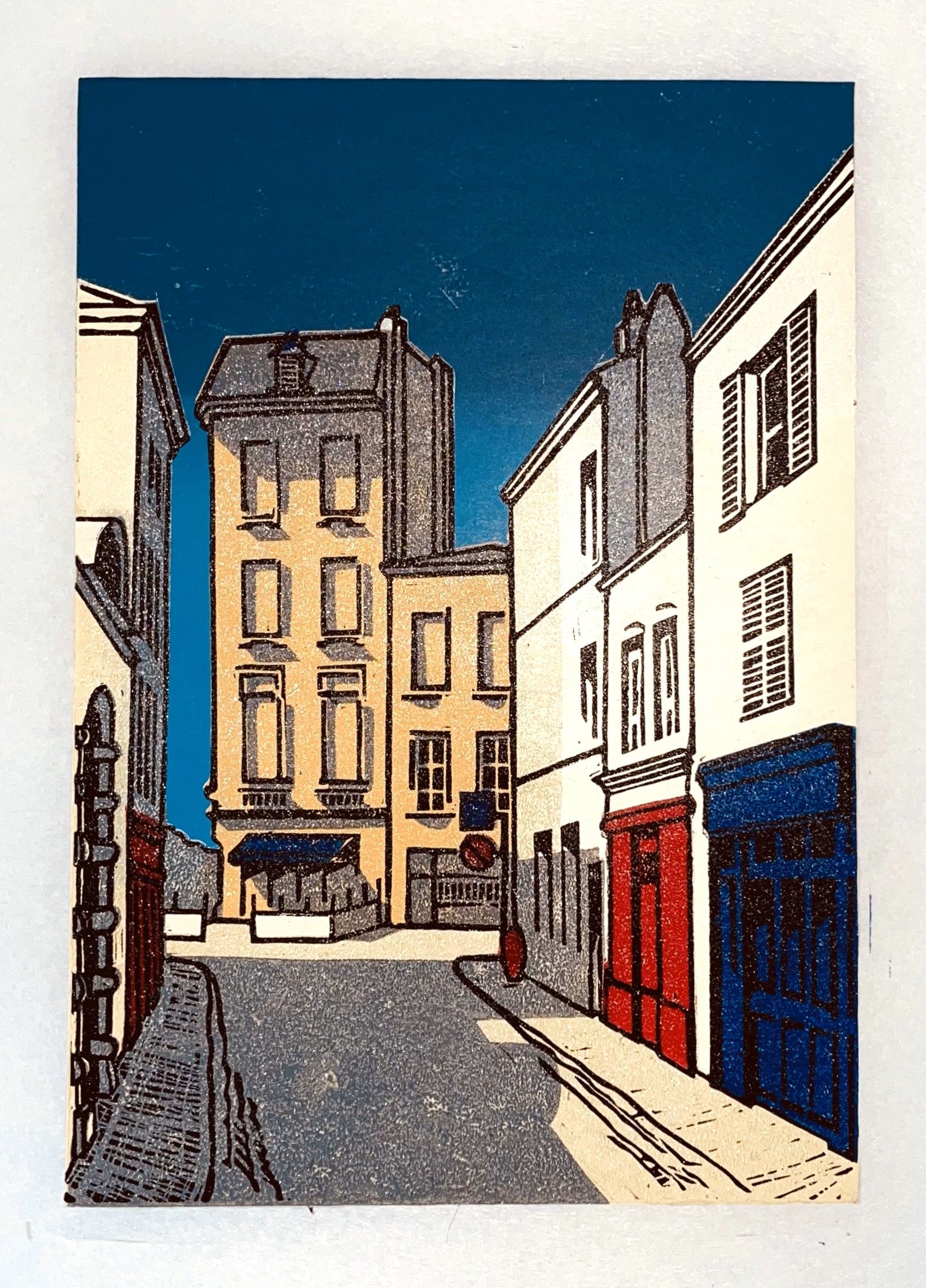 Straatbeeld met gebouwen, blauwe lucht en rode en blauwe winkelgevels.