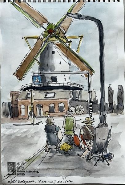 Mensen zitten buiten bij een café rond een windmolen, met hoge wieken en een donkere sluis op de achtergrond.