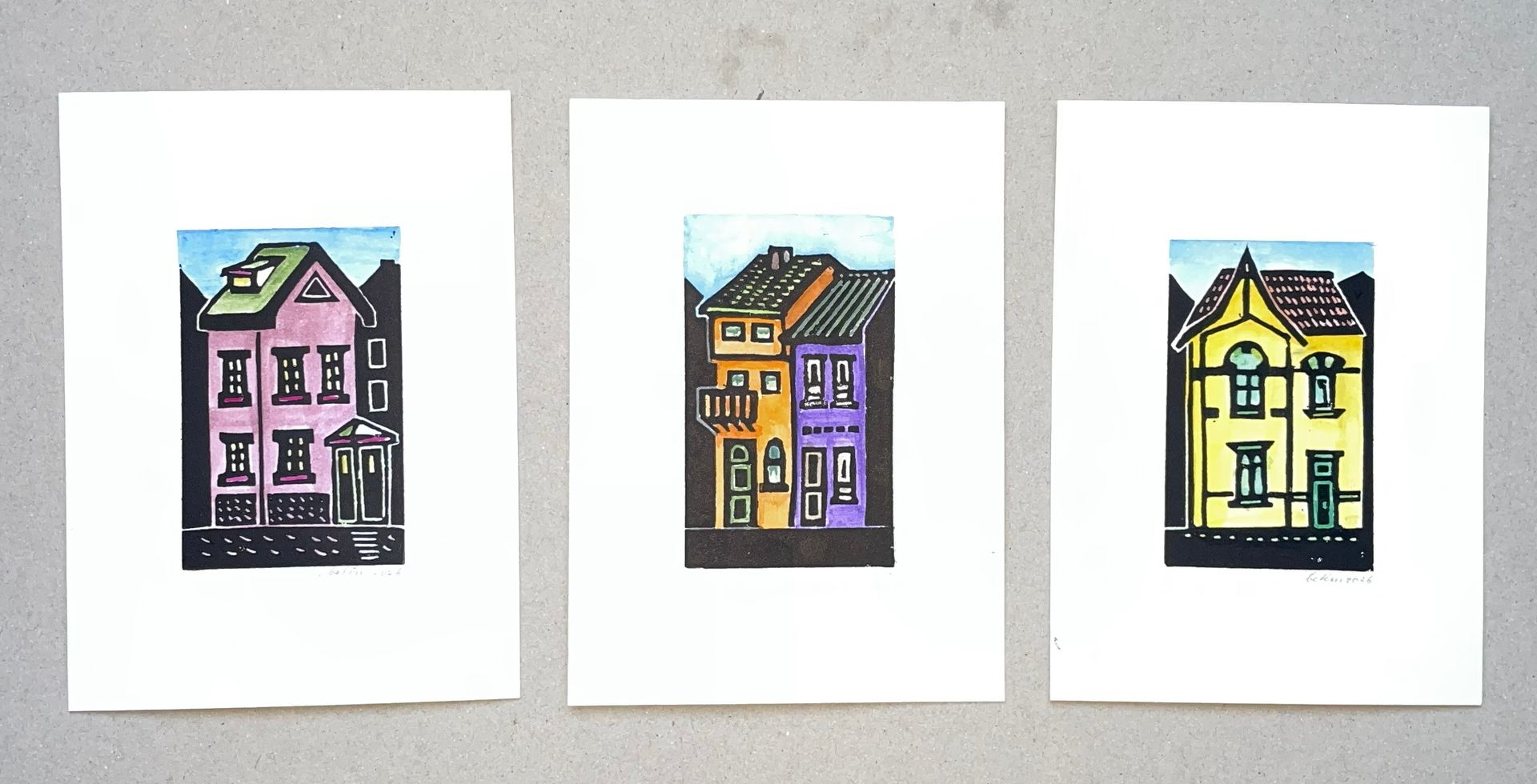 Drie kleurrijke, gestileerde ingekleurde linoprints van huizen op een witte achtergrond.