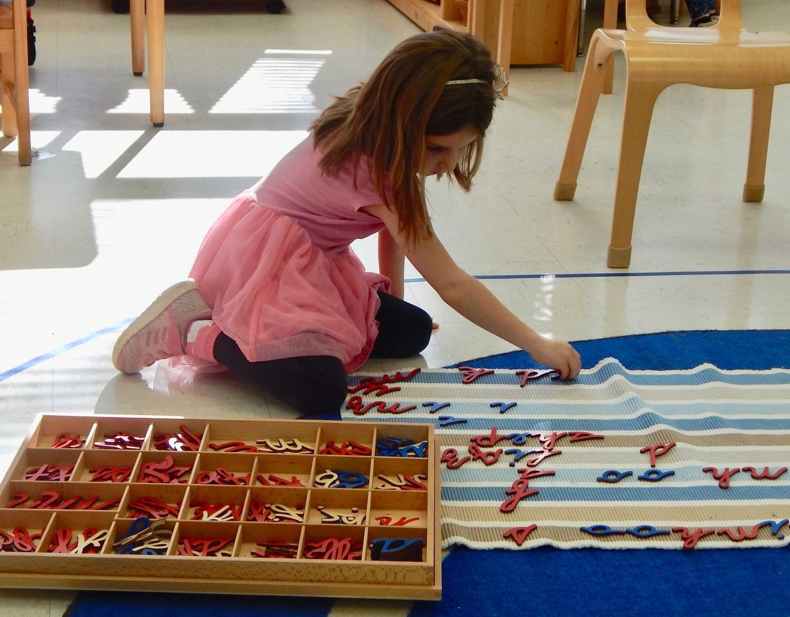 A little girl in a pink dress is playing with alphabet letters