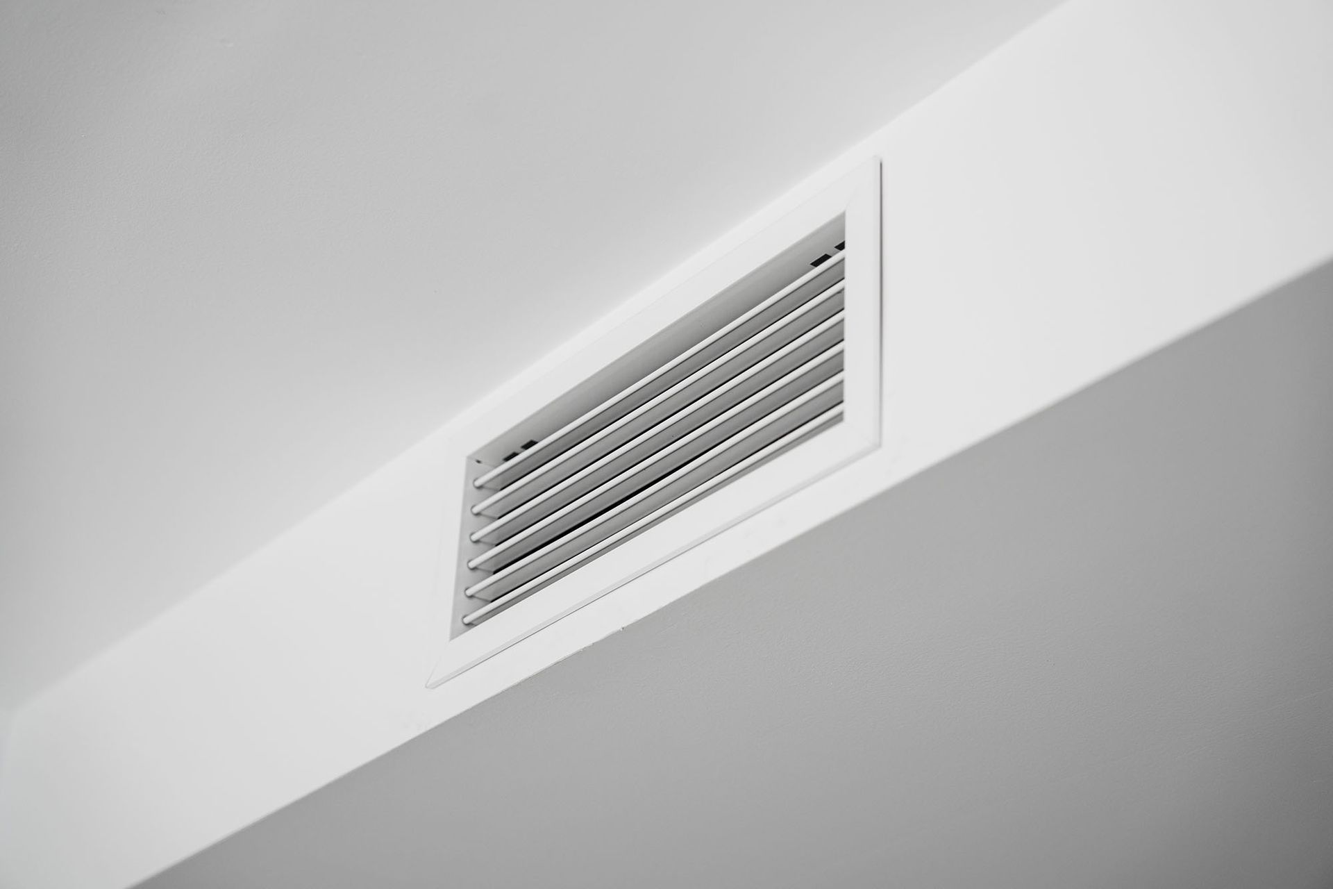 White ceiling air vent with horizontal slats on a light gray wall