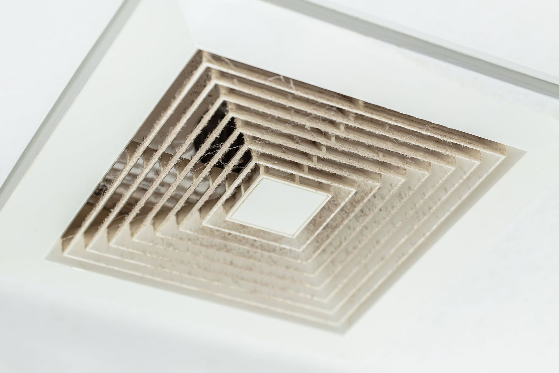 Square white ceiling vent with a central opening and layered wooden slats, viewed from below
