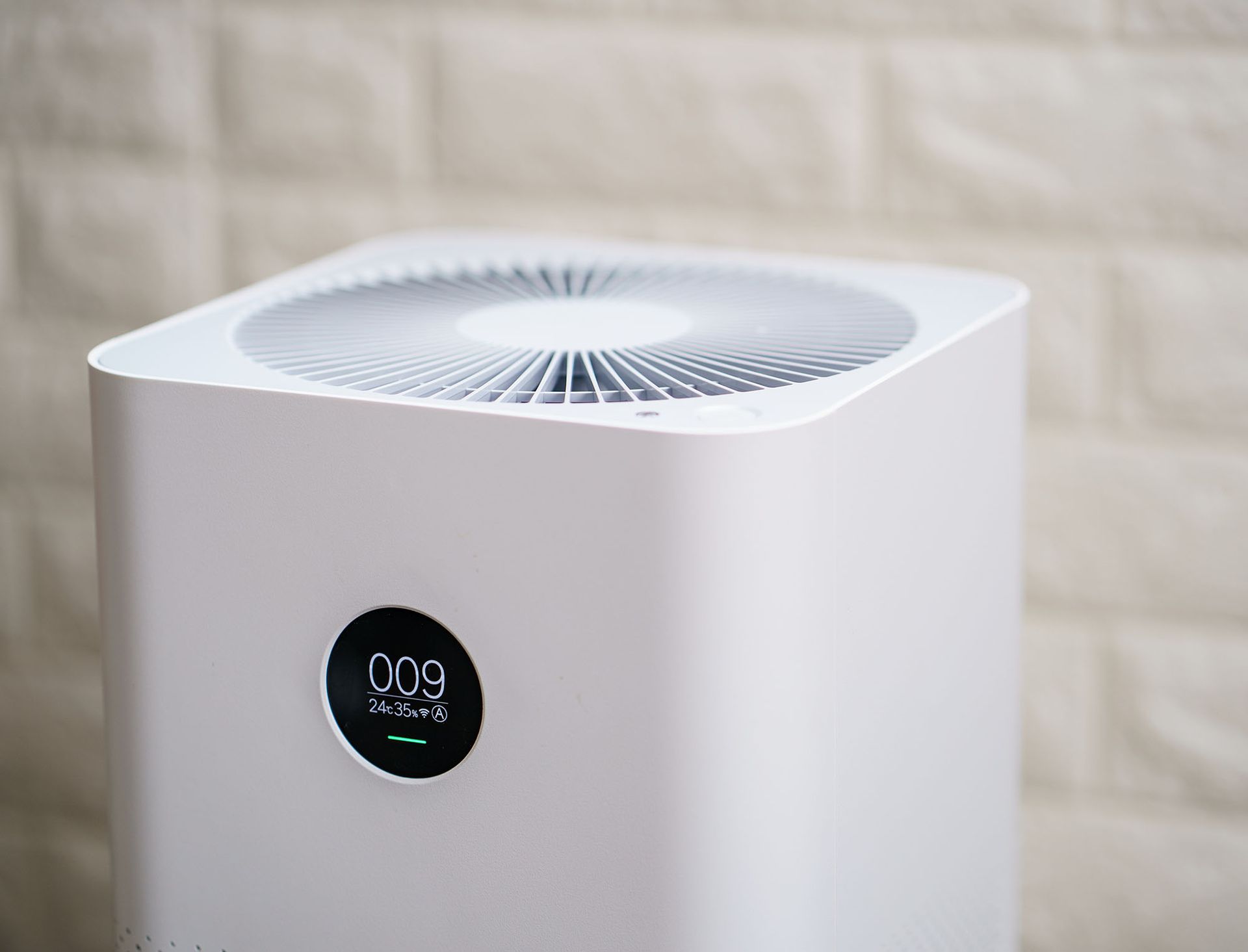 White air purifier with a round display and top vent against a light wall