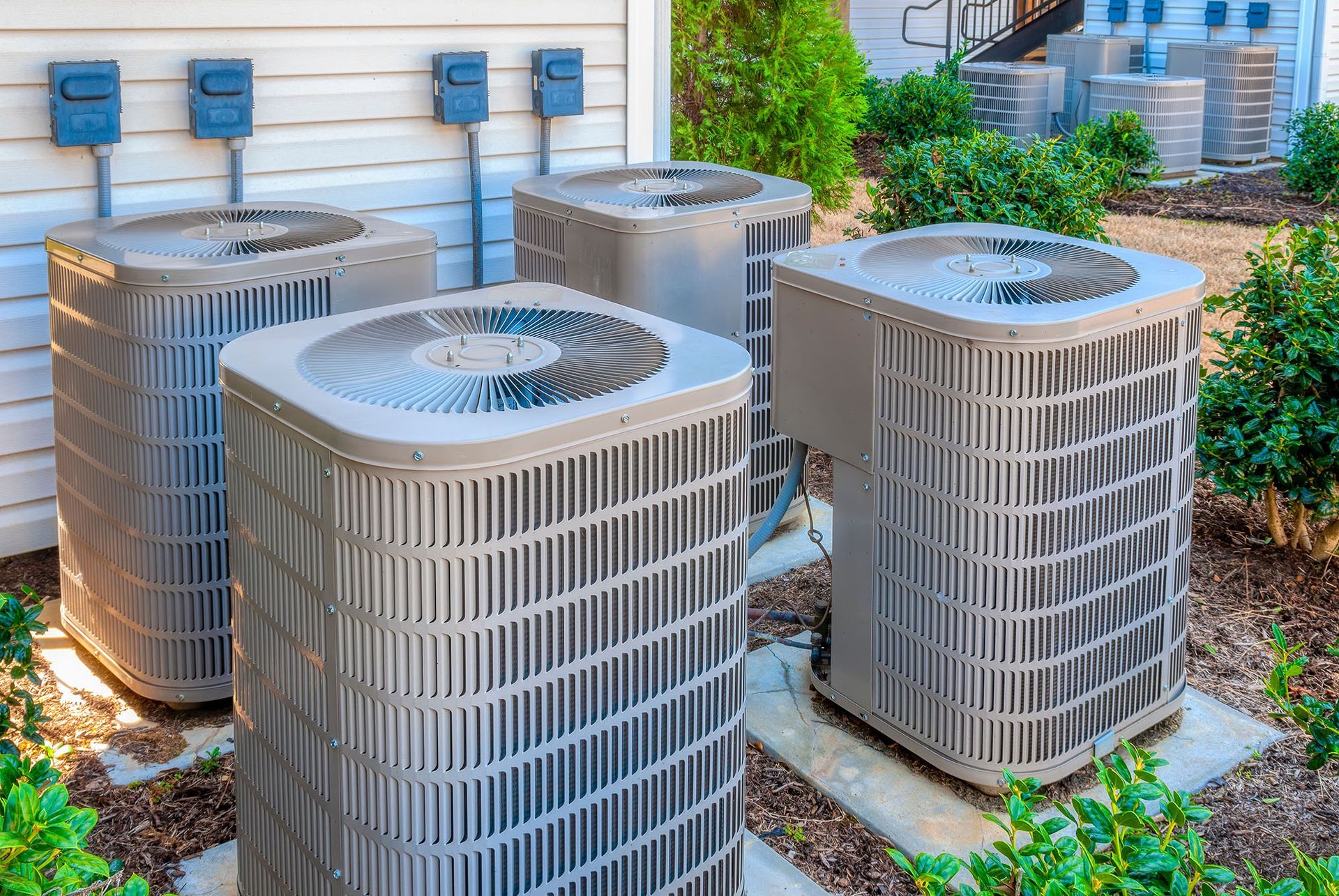 Three outdoor HVAC units beside a house, with vents and gravel around them
