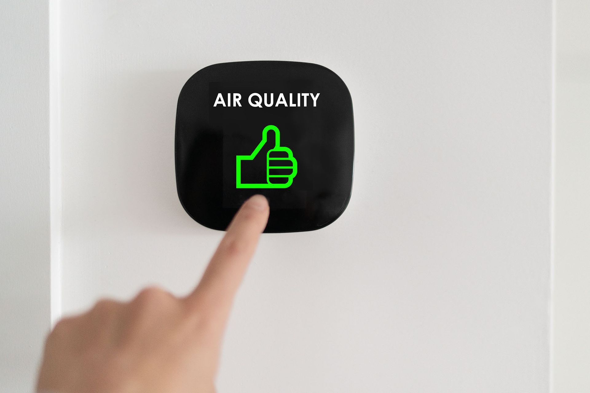 Finger pressing black air quality sensor with green thumbs-up icon and “AIR QUALITY” text