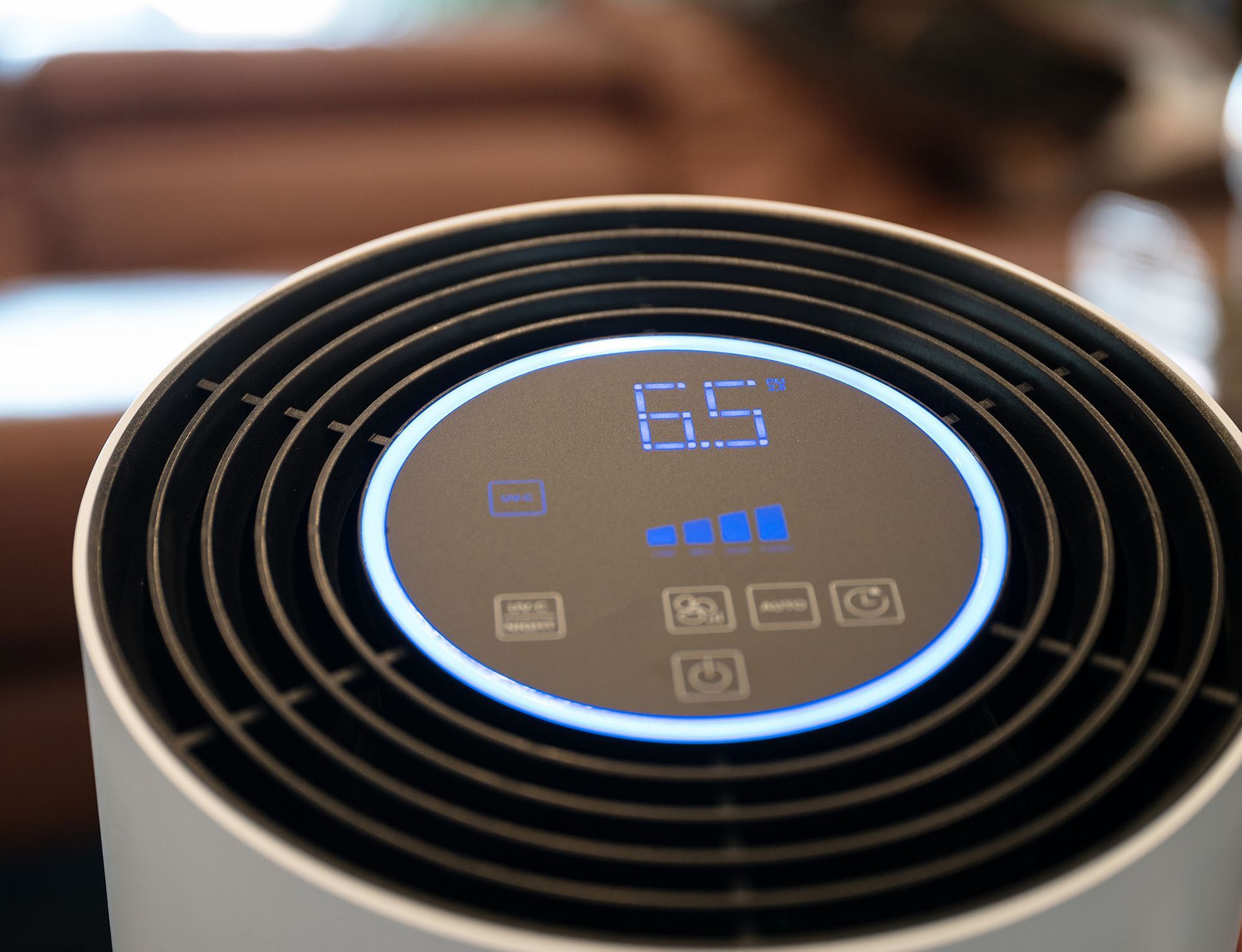 Close-up of a black round air purifier display showing 65 and blue indicator lights.
