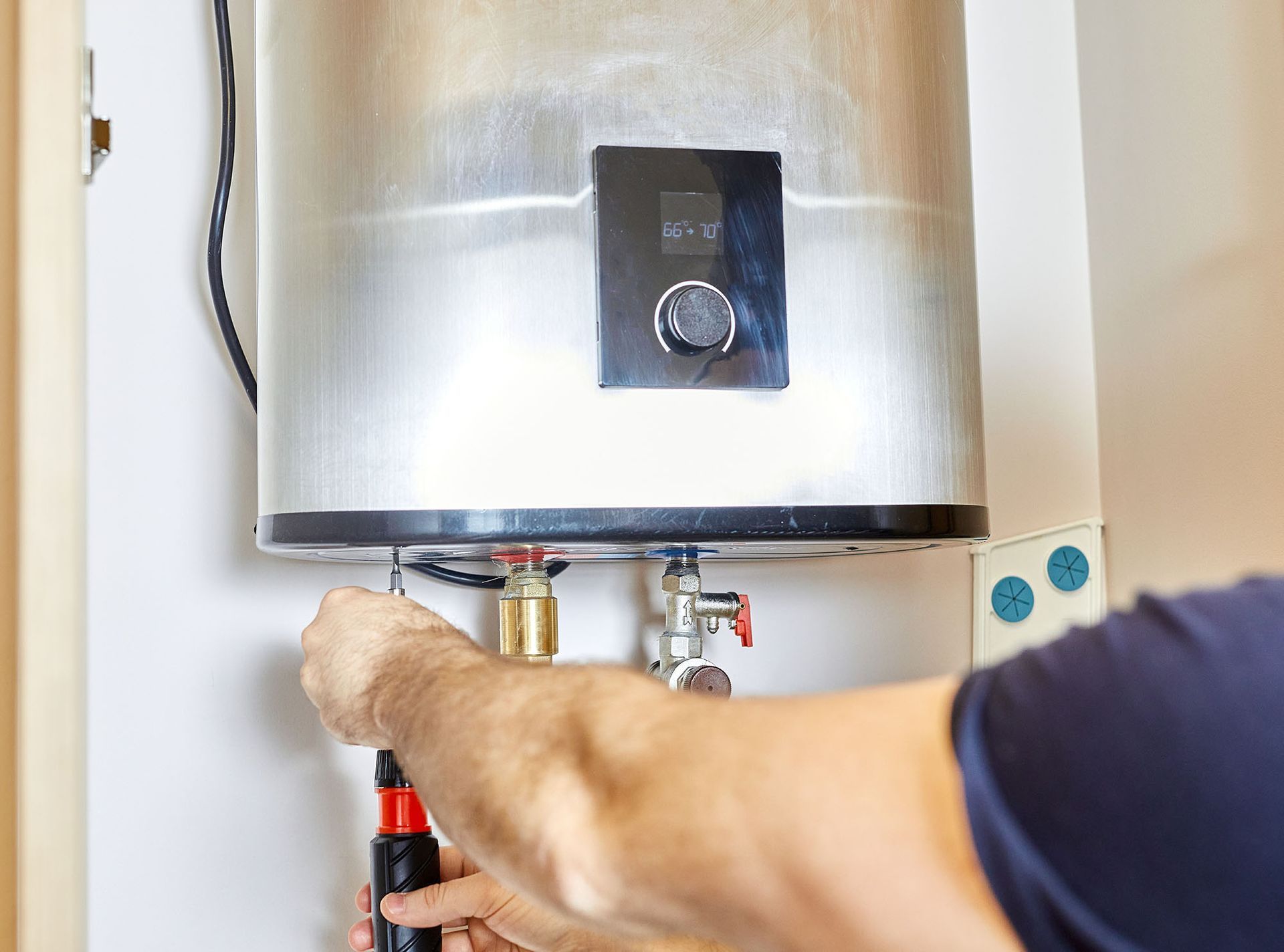 Hands adjusting pipes under a silver water heater with a control panel.