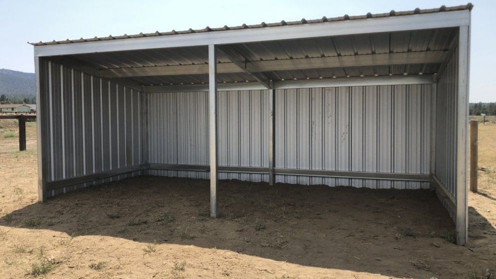 A metal shed is sitting in the middle of a dirt field.