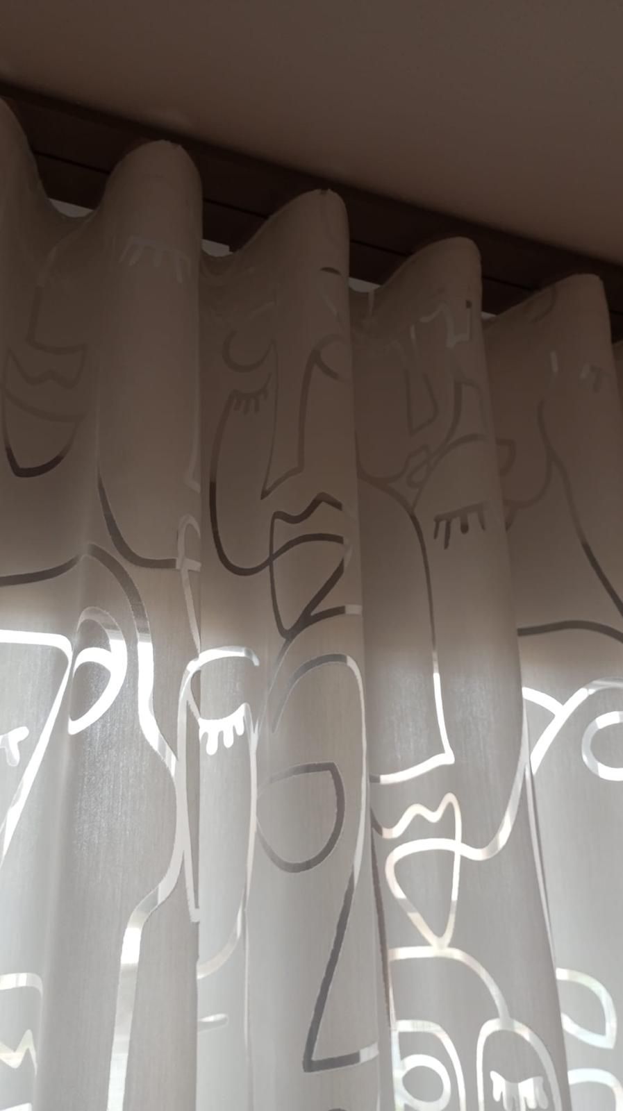 Tenda bianca con motivi ripetuti a forma di foglie grigie e riflessi di luce verticali vicino alla parte superiore di una finestra