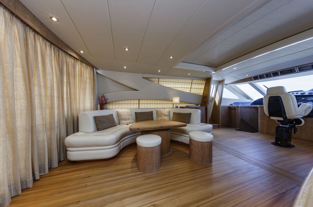Salone moderno di uno yacht con divano bianco curvo, pouf rotondi, pavimento in legno e ampie finestre.