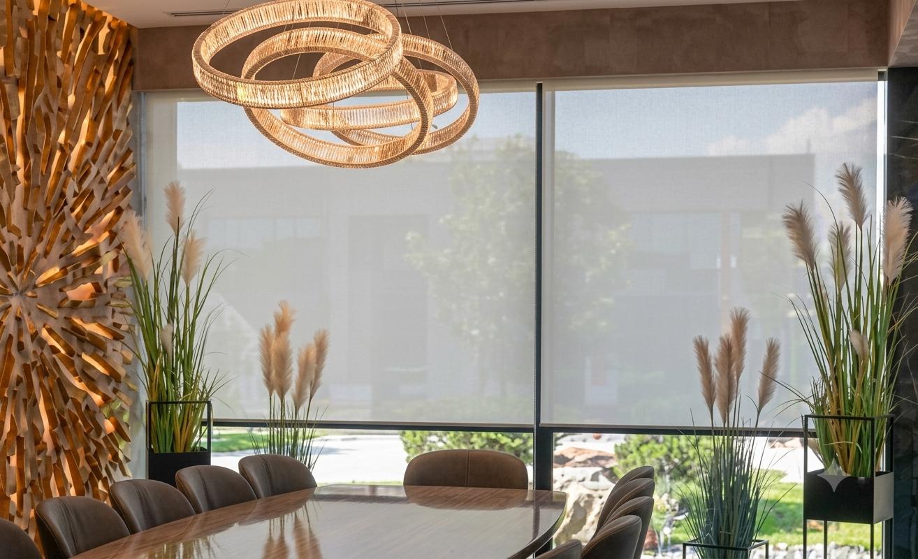 Sala conferenze moderna con tavolo in legno, lampade a sospensione intrecciate e piante alte vicino alle grandi finestre.