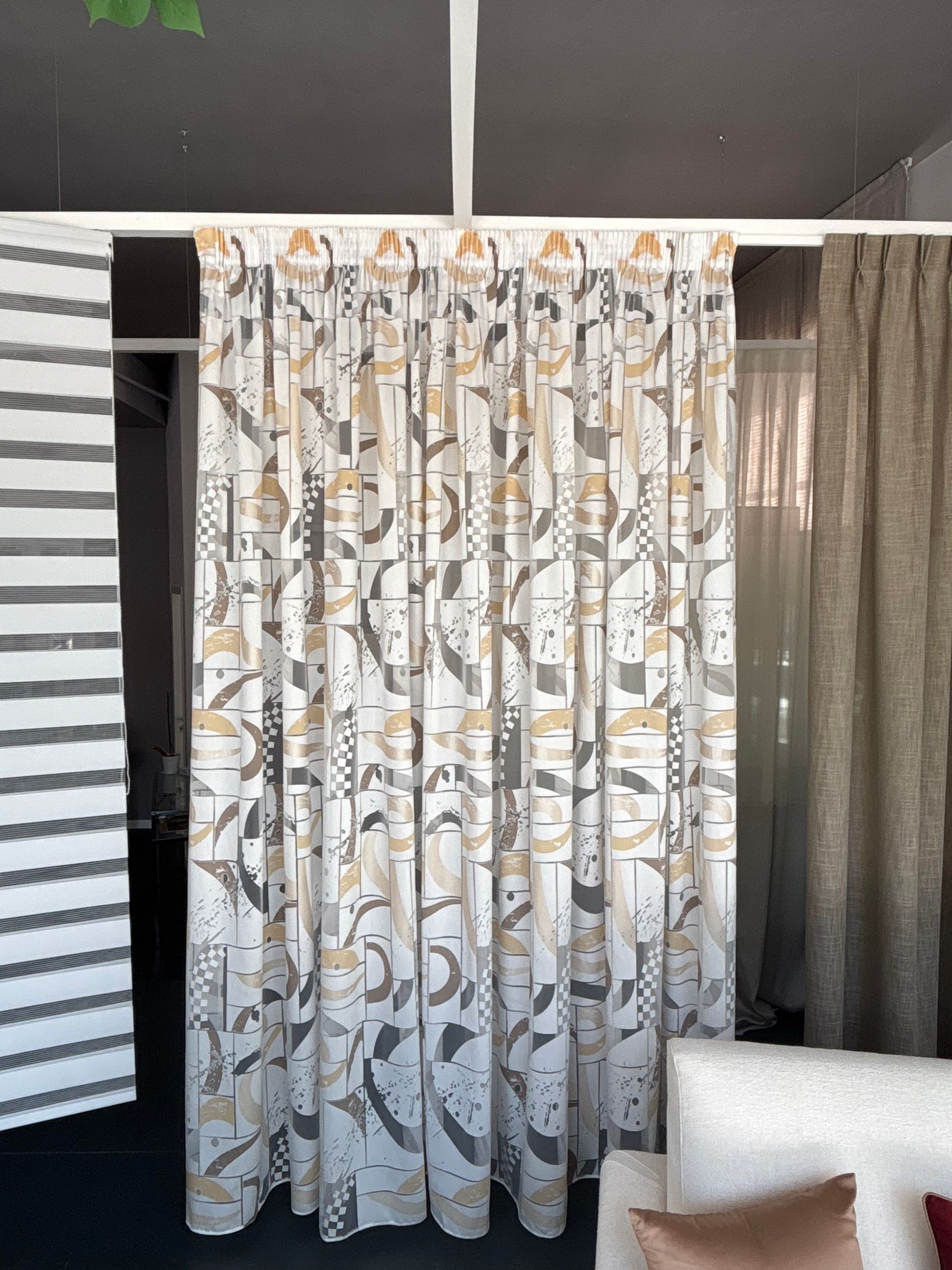 Tende decorate in una stanza accanto a una parete a righe bianche e nere e una sedia beige.
