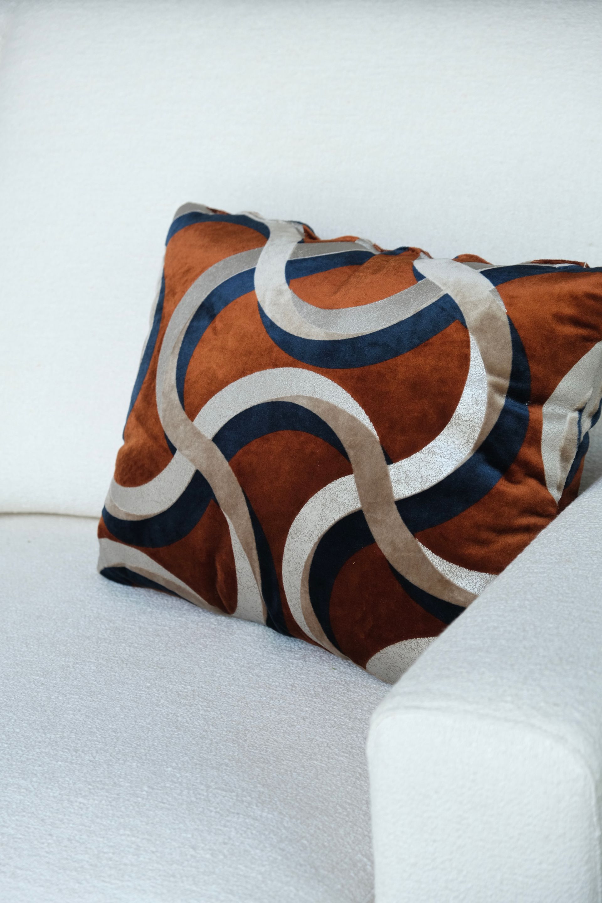 Cuscino decorativo a fantasia arancione, blu e beige su un divano bianco.