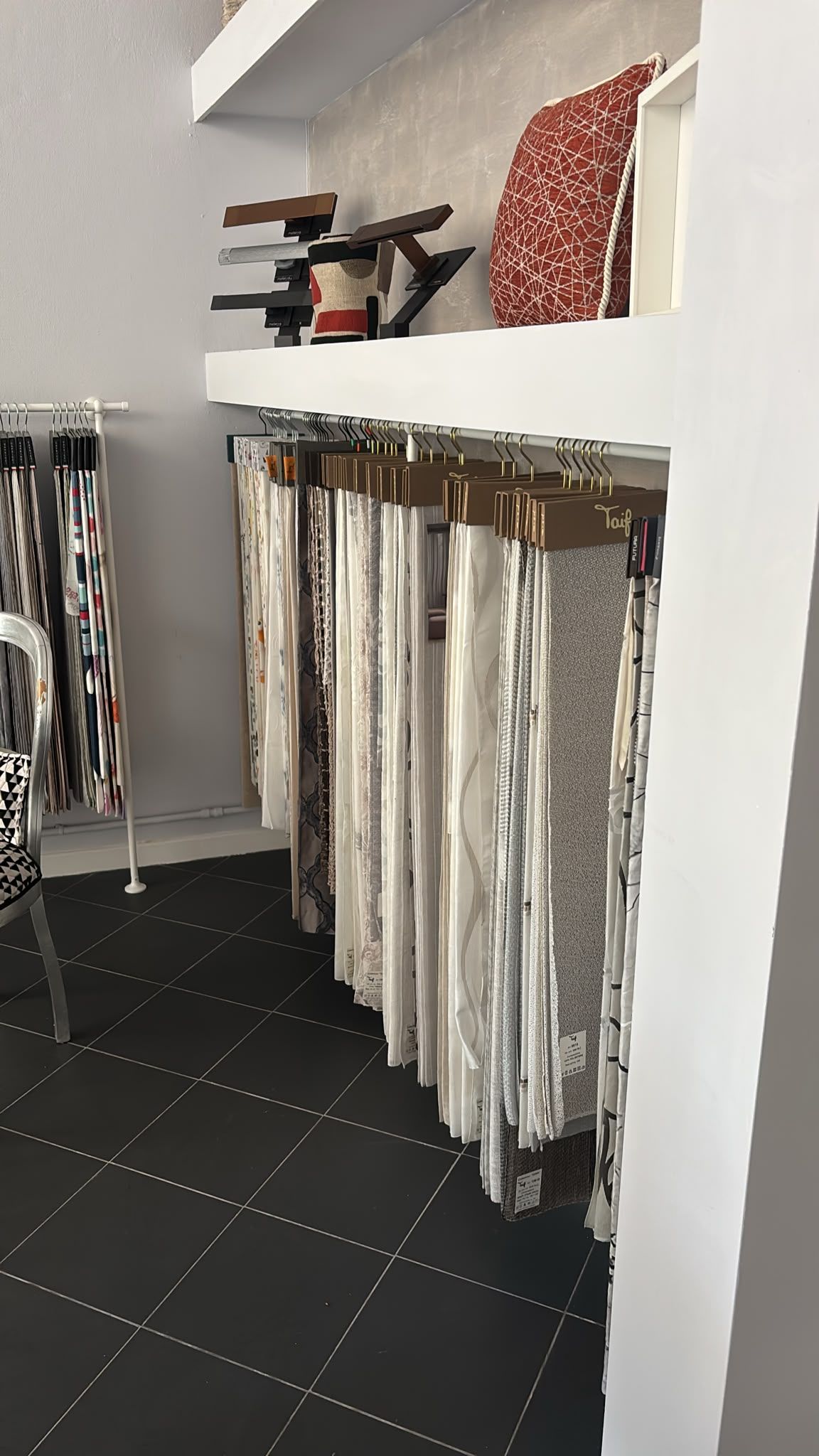 Scaffale di un negozio di abbigliamento con camicie piegate e capi appesi sopra e sotto una nicchia espositiva bianca.