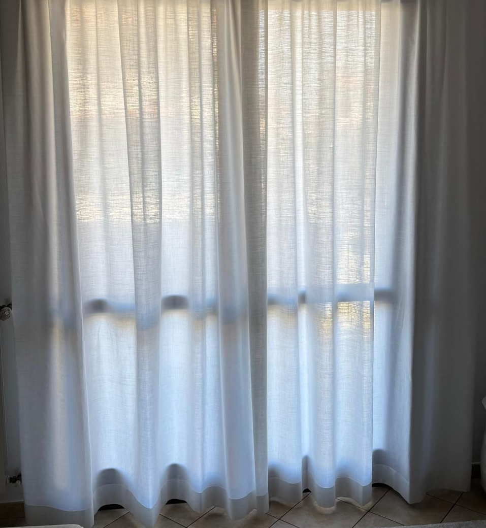 Tende bianche trasparenti che coprono una finestra, delicatamente illuminata dalla luce del giorno.