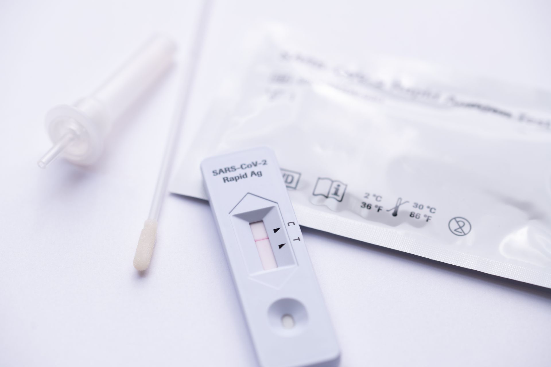 Schnelltestkit für COVID-19 mit Testkassette, Abstrichtupfer und Gebrauchsanweisung auf weißer Oberfläche