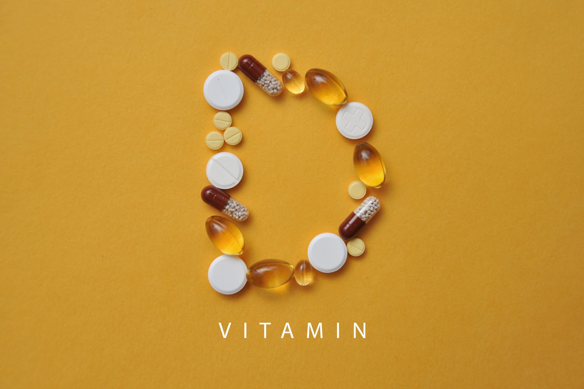 Vitamin, geschrieben mit Kapseln und Pillen auf senfgelbem Hintergrund