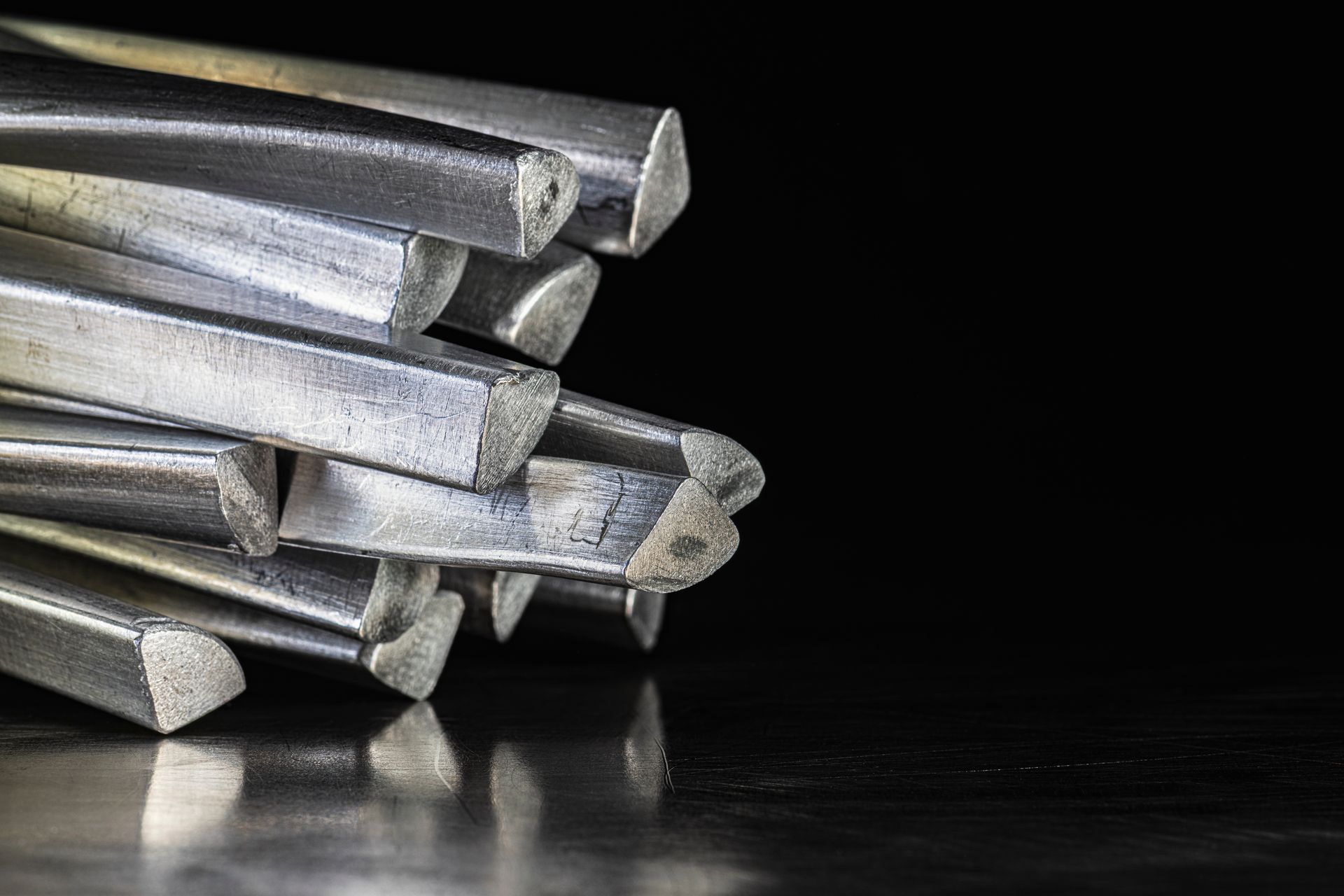 Stack of metal rods or bars arranged on a dark surface against a black background.