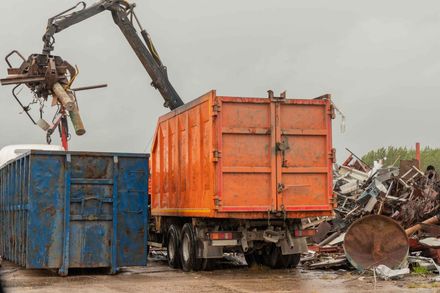 A dump truck is being loaded with scrap metal by a crane.