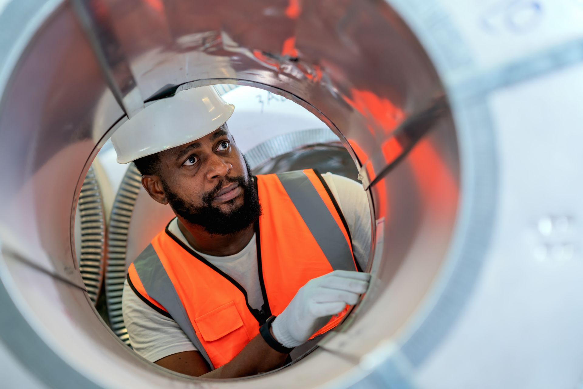 A male warehouse worker is examining the surface of steel coils in a factory.