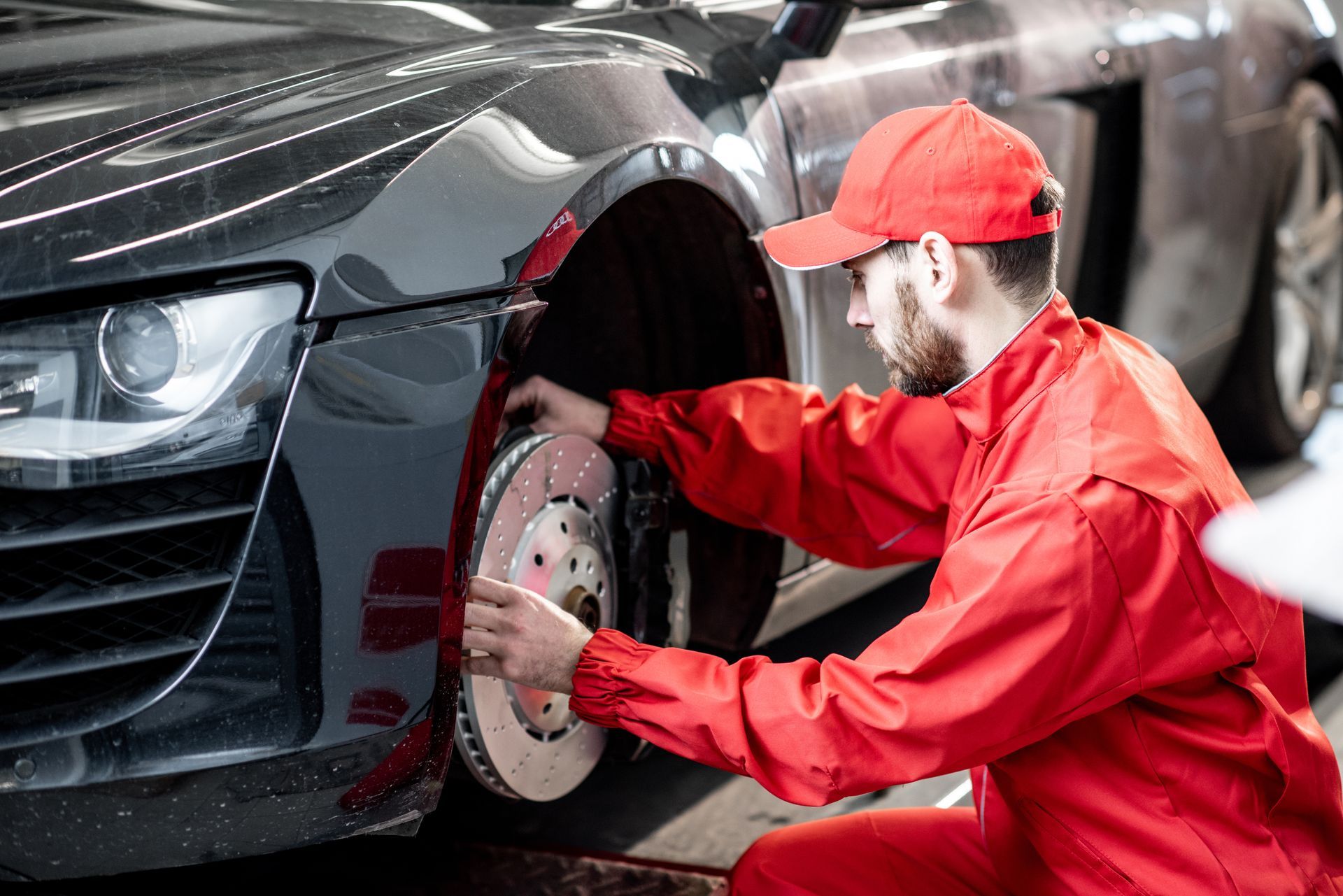A mechanic in a red uniform is performing Mercedes-Benz auto repair, checking the front brakes. A mechanic in a red uniform is performing Mercedes-Benz auto repair, checking the front brakes.