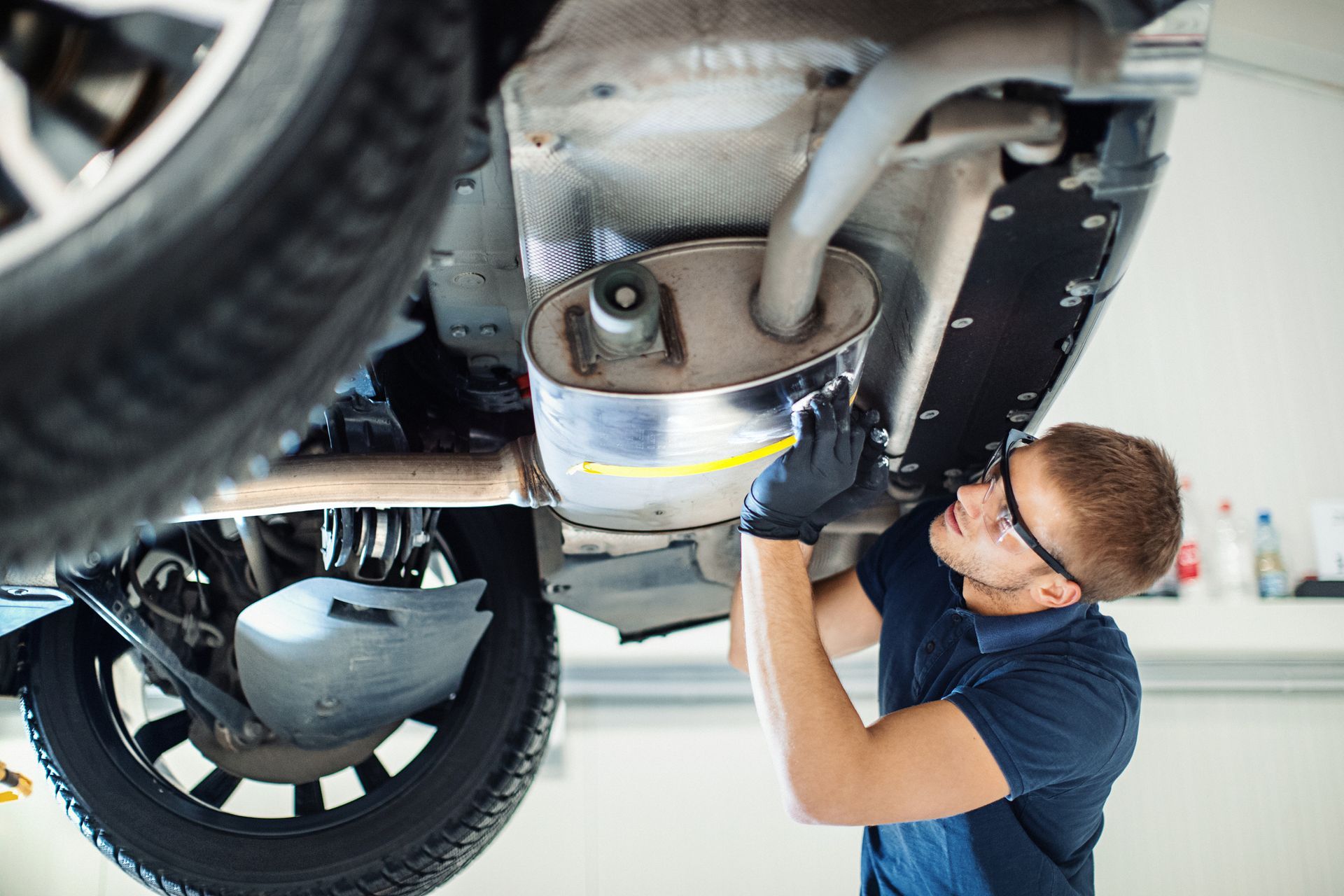 A mechanic is performing a Mercedes-Benz car repair by checking the lower section of the vehicle.