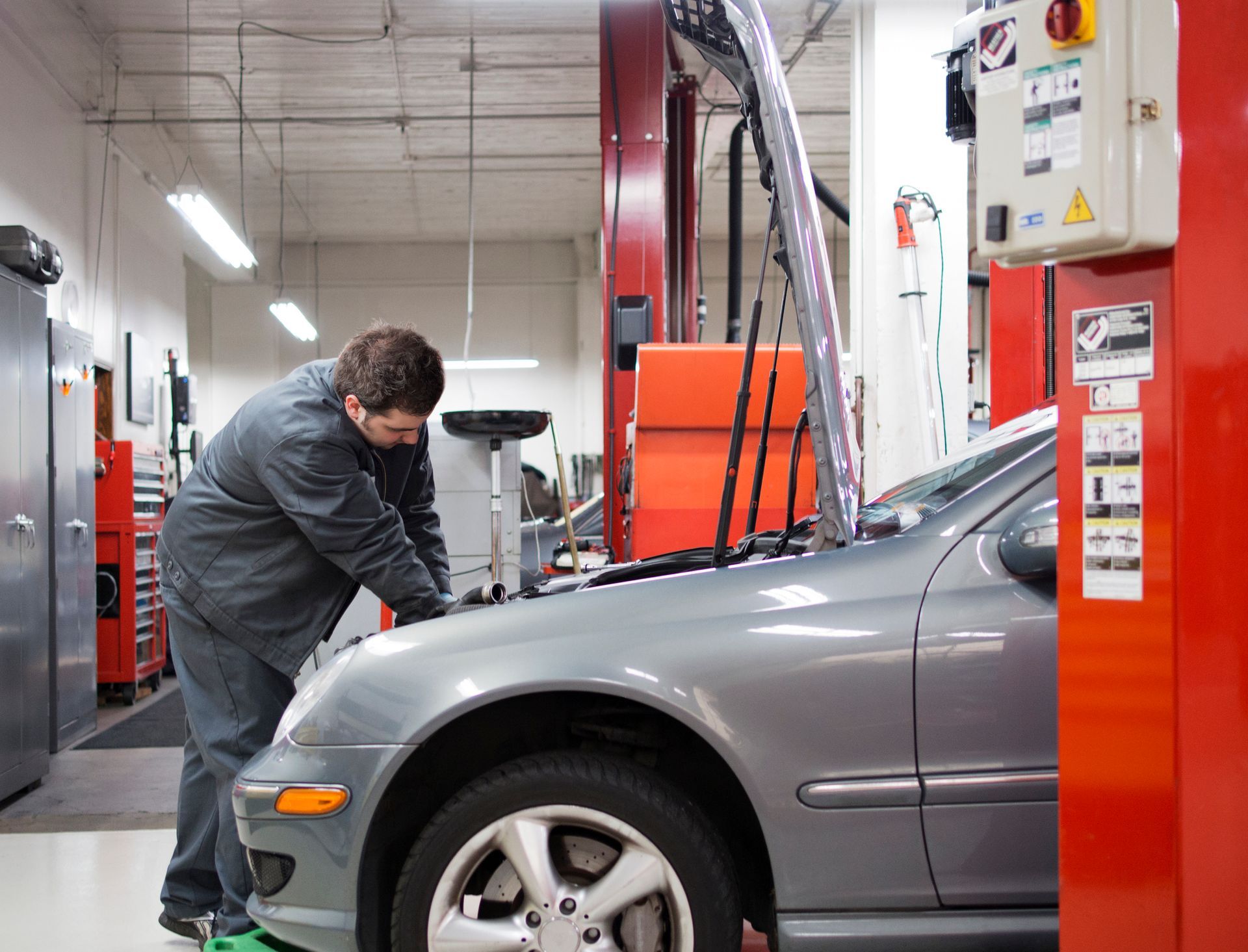 A mechanic performing Mercedes-Benz auto repair in a garage, surrounded by tools and equipment.