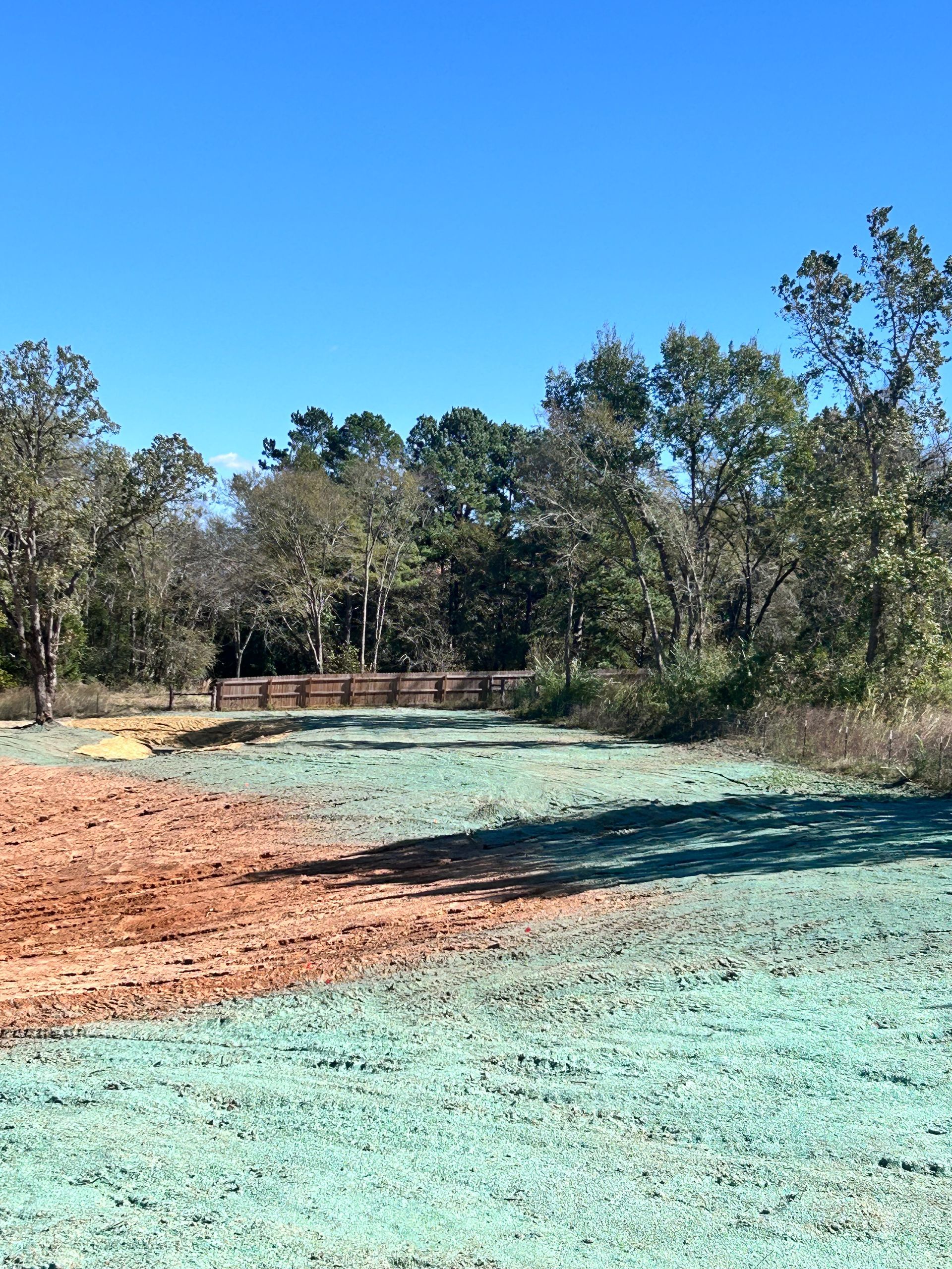 A field with brown and green areas, trees in the background, blue sky.