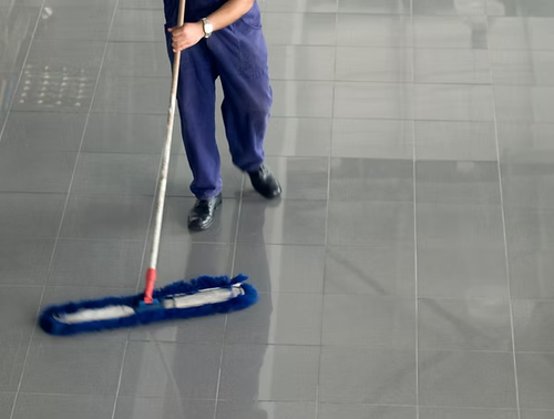 Janitor in blue uniform mopping a large grey tiled floor
