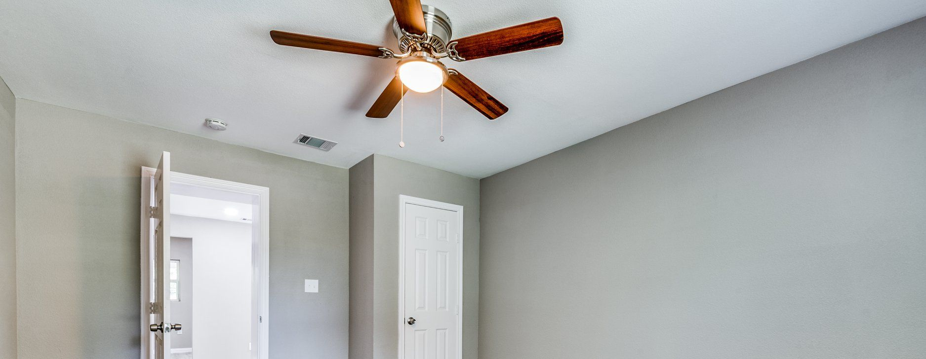Empty gray room with ceiling fan, white trim, and a partially open door.