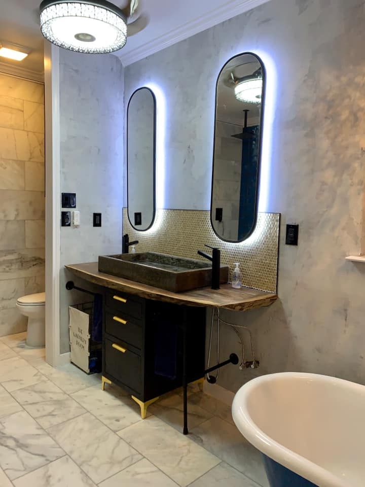 Modern bathroom with black vanity, two backlit oval mirrors, and a freestanding tub.