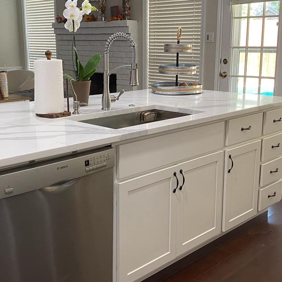 Kitchen island with white cabinets, marble countertop, stainless steel sink and appliances.