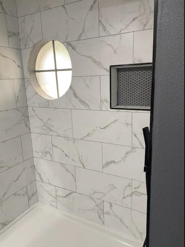 Tiled shower with marble-like pattern.  An oval window and recessed shelf are set into the walls.
