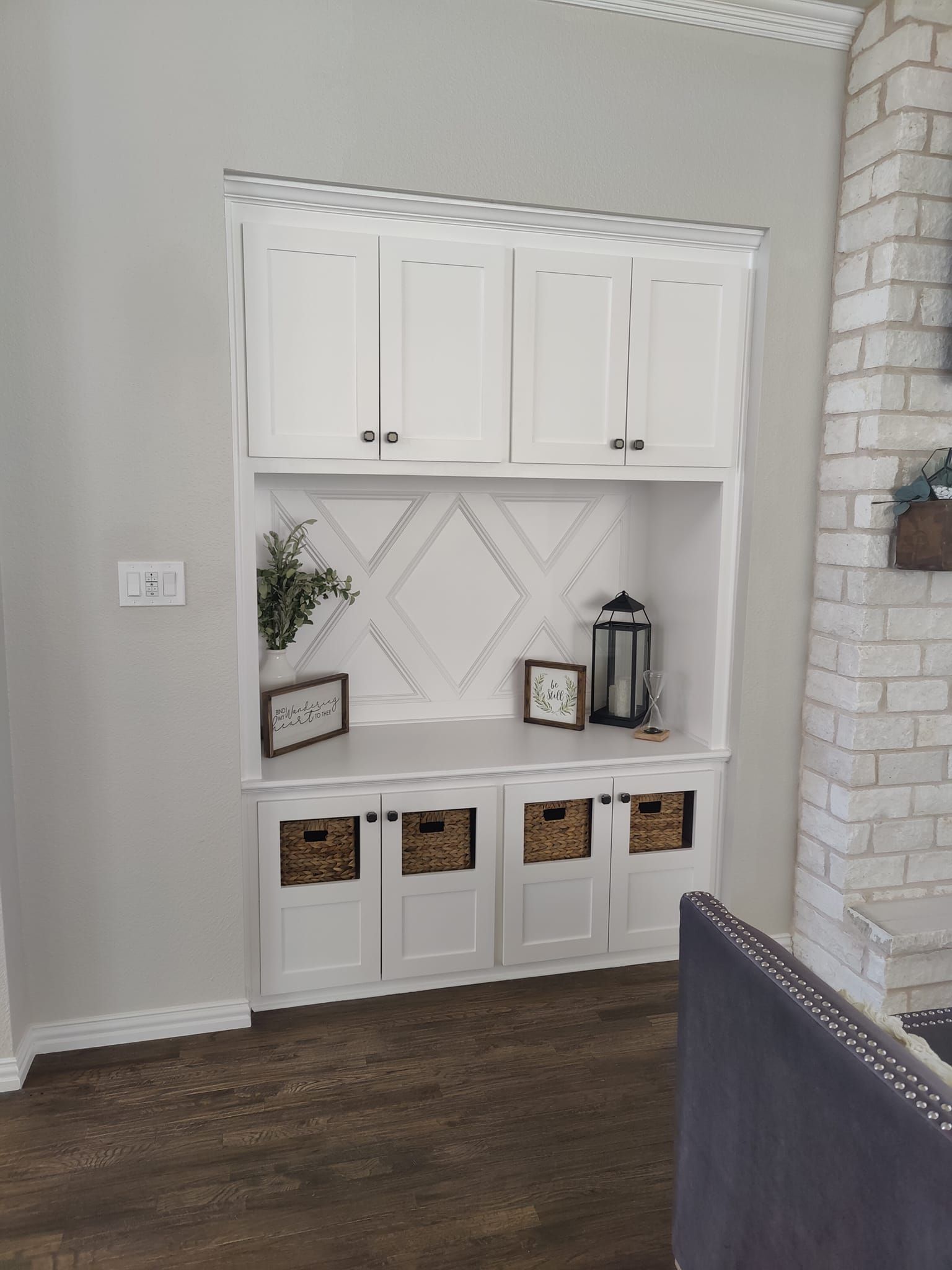Built-in white storage unit with cabinets, shelves, baskets, and decorative items.