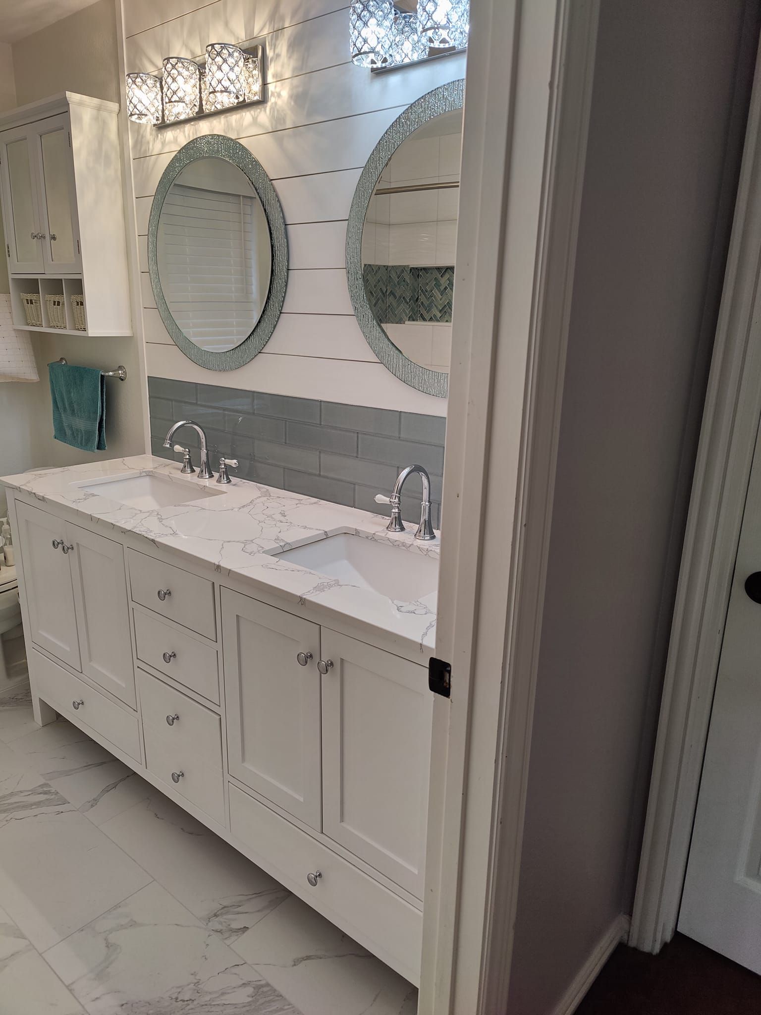 White bathroom with double vanity, oval mirrors, and blue tile accent wall.